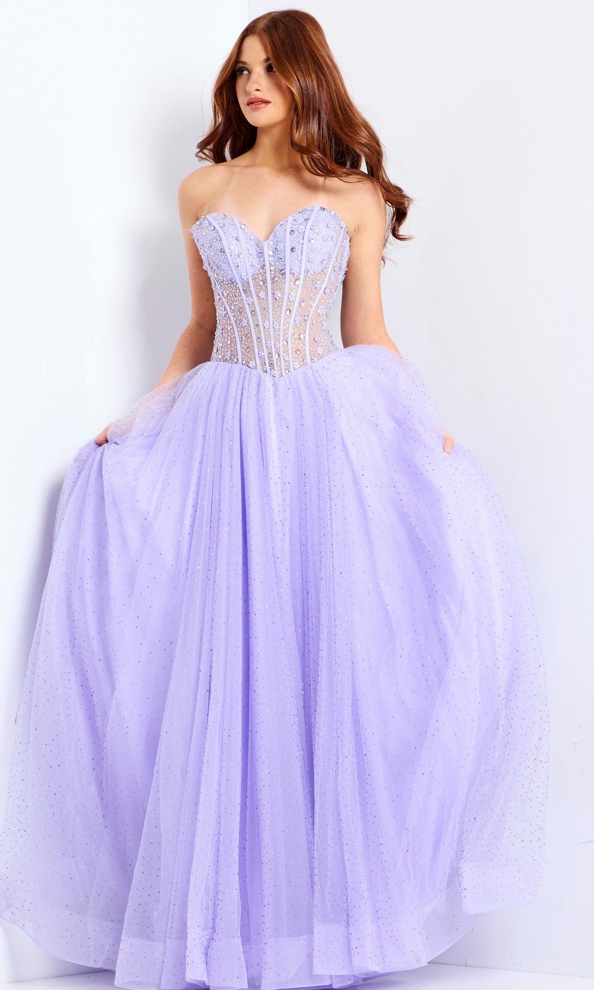 A woman wears the Jovani 48309 long prom dress, featuring a strapless, sheer beaded corset bodice and a full tulle skirt, standing against a white background.